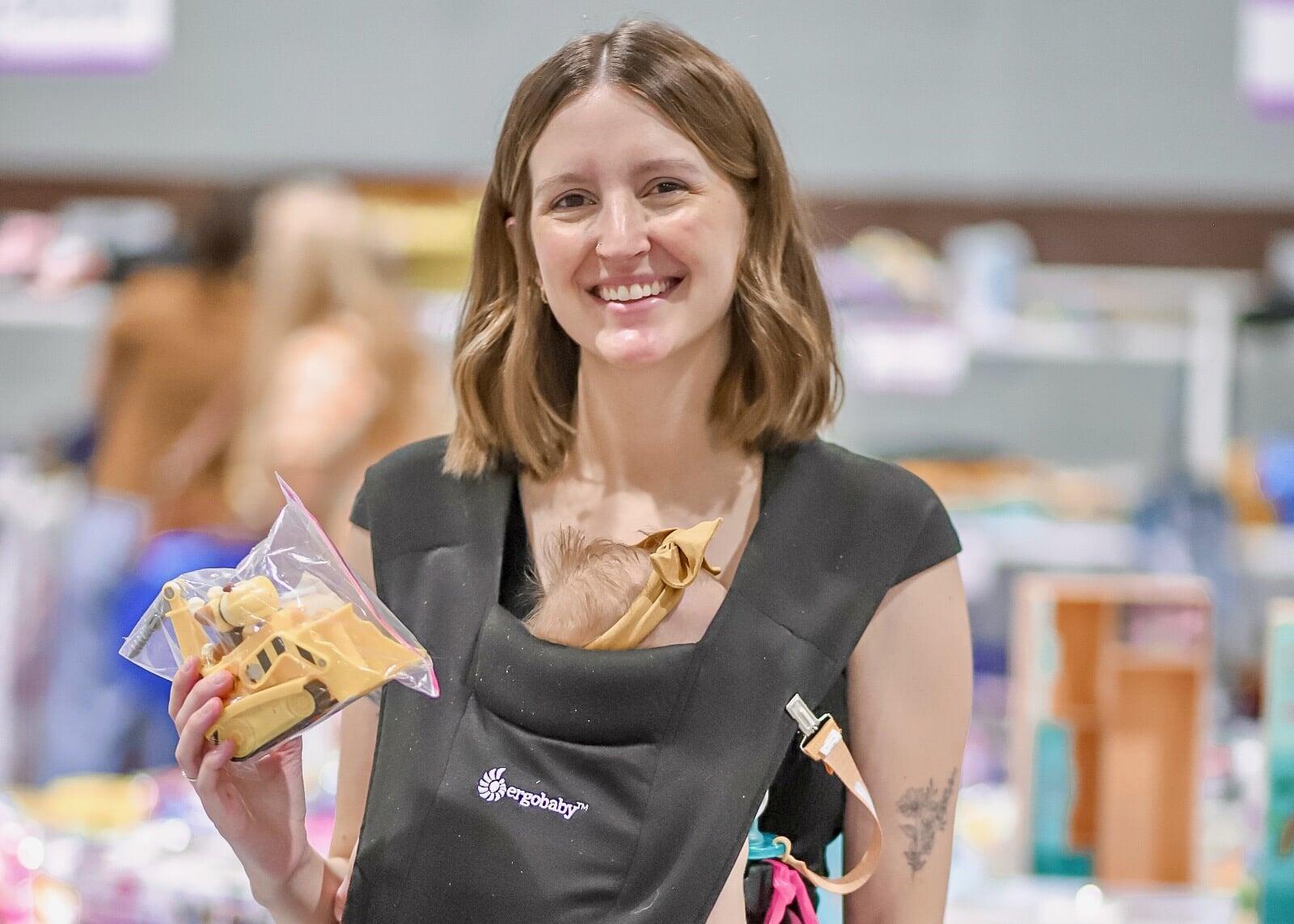A smiling woman shopping is surrounded by tables full of toys.