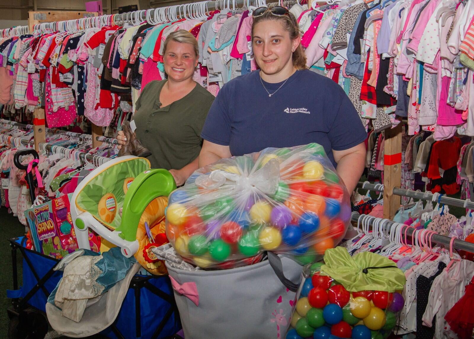 A couple with their arms around each other shopping at the JBF sale. The lady has some infant clothing hanging on her arm.