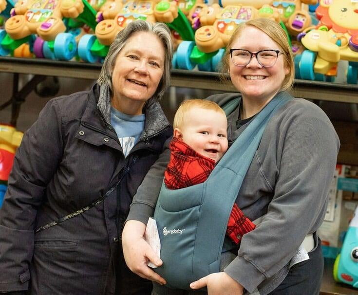 A couple with their arms around each other shopping at the JBF sale. The lady has some infant clothing hanging on her arm.