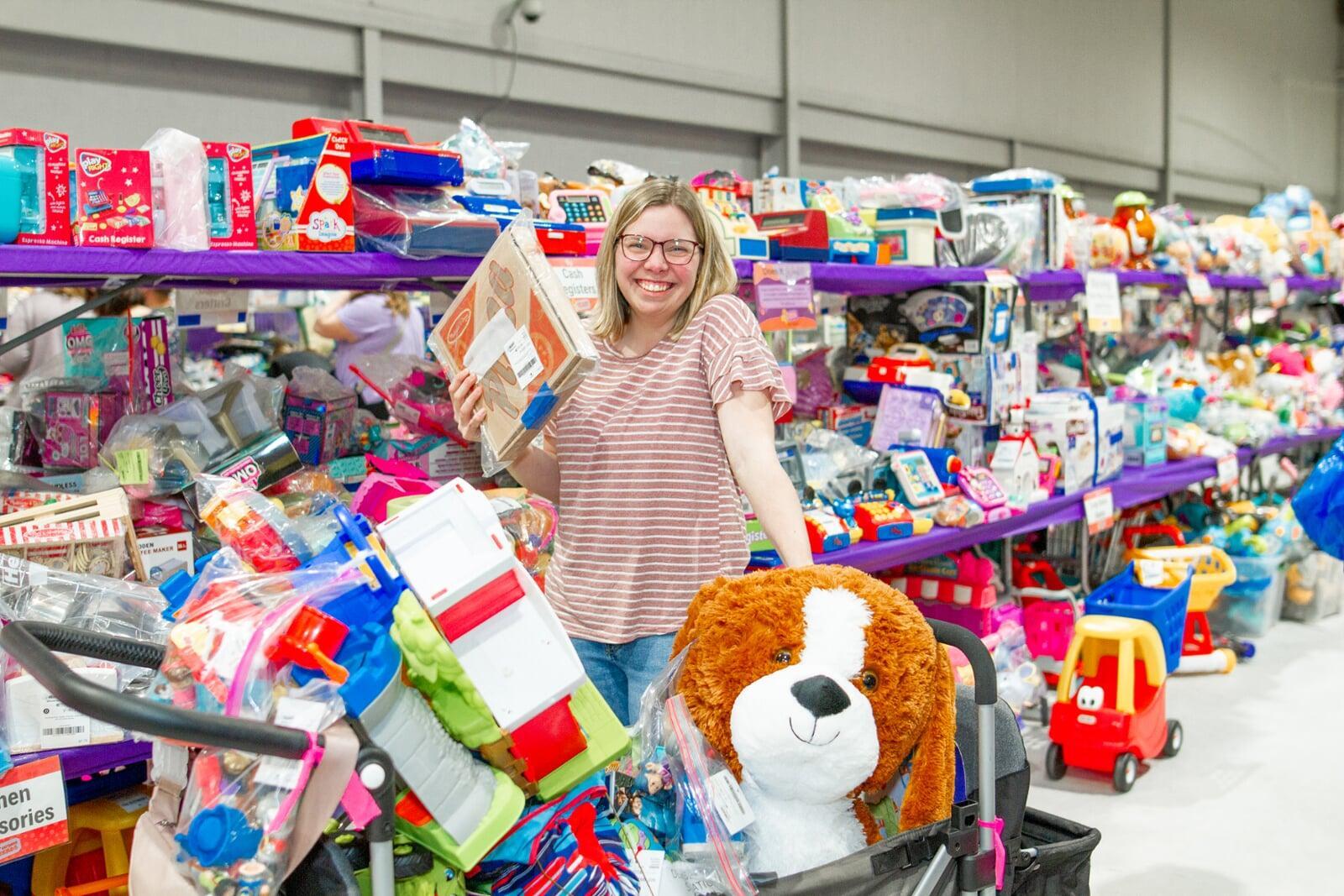 A smiling woman shopping is surrounded by tables full of toys.