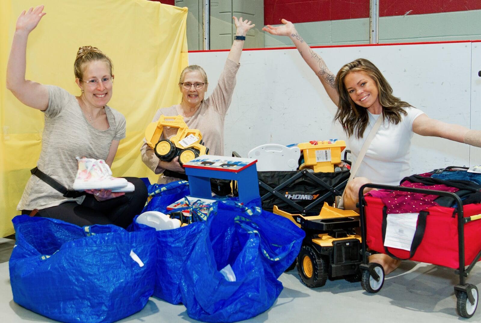 Three women sitting on the floor going through blue Ikea bags full of items.