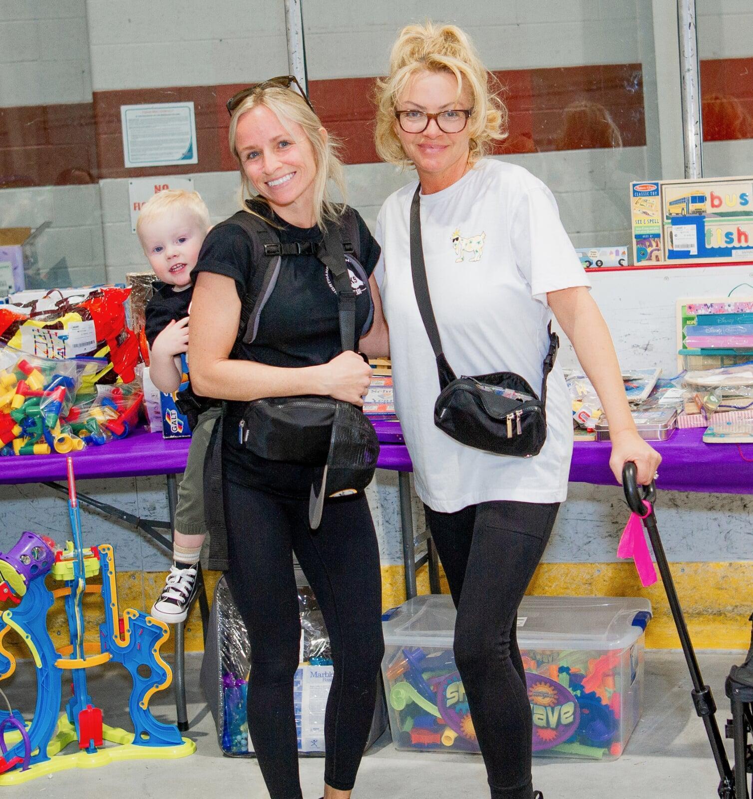 Two women shopping. One is pulling a wagon and the other has a child in a backpack carrier.