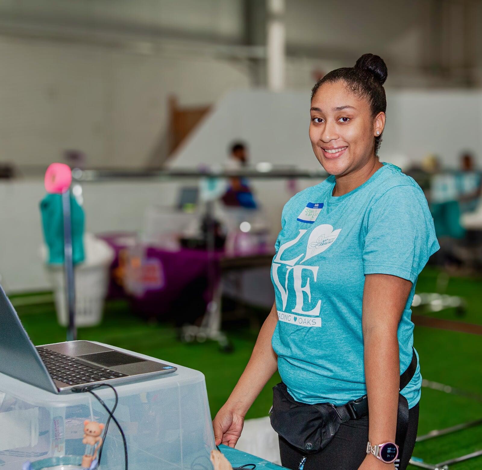A JBF Retail Sales Specialist standing at her cash register. She is wearing a teal blue JBF Love shirt.