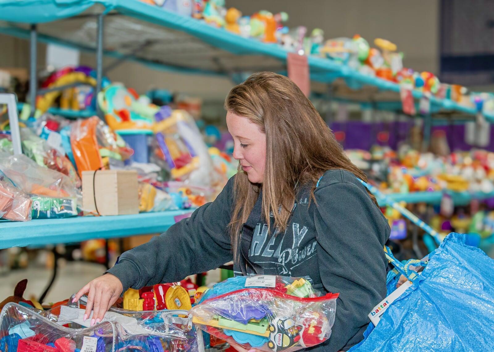 A smiling woman shopping is surrounded by tables full of toys.
