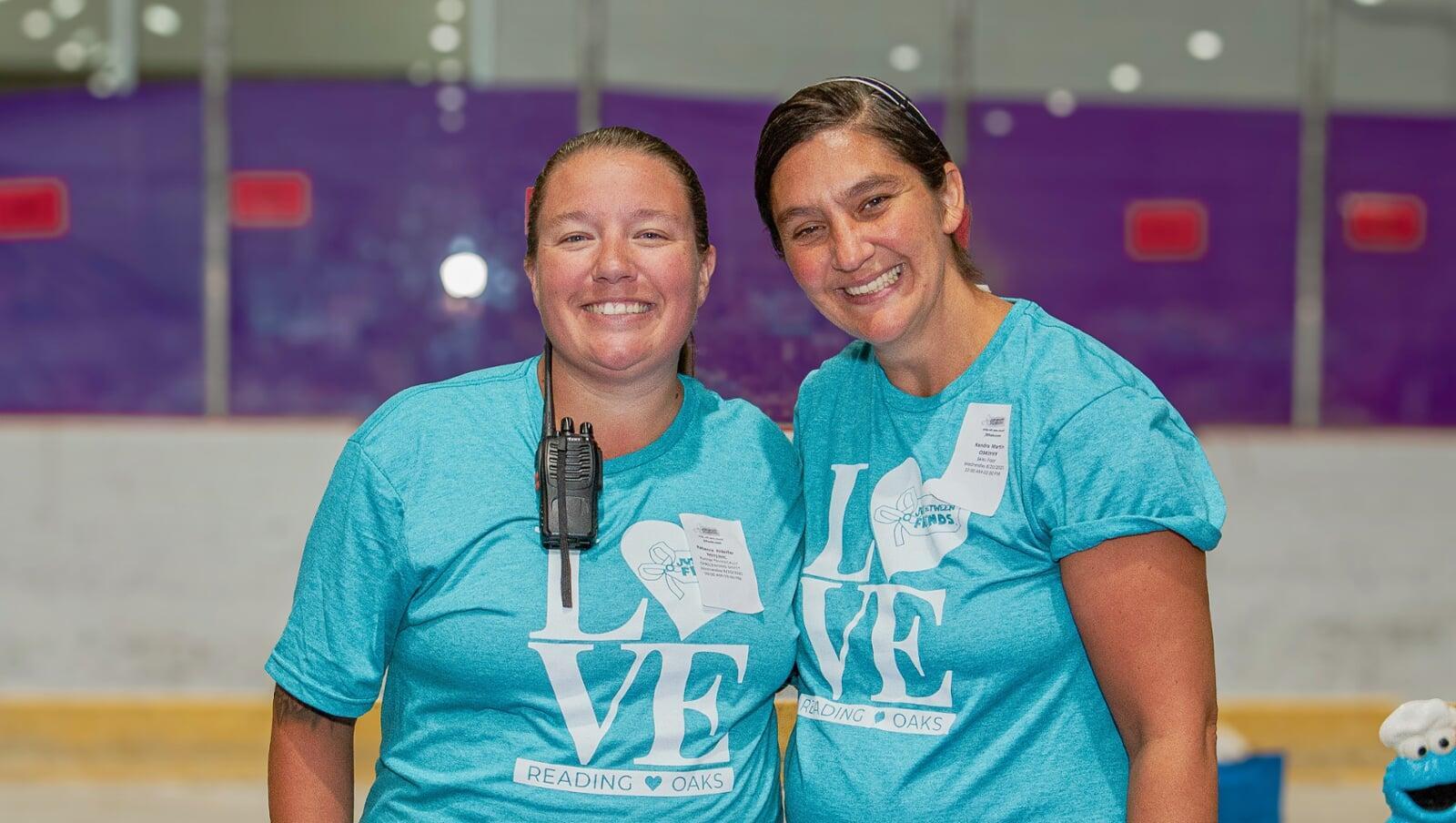 Two woman working together in the ice-rink hold are wearing teal blue JBF Love shirts